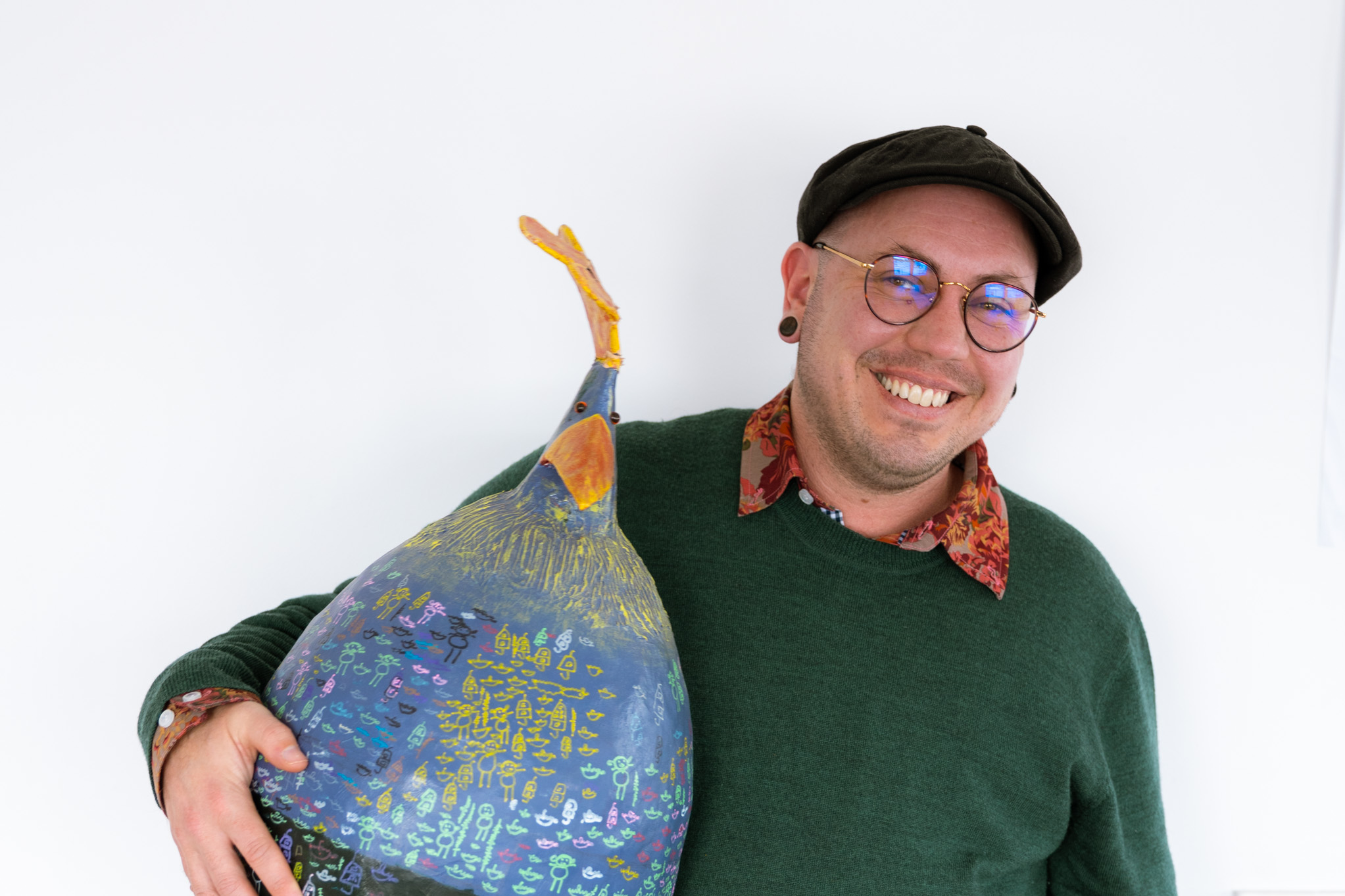 Stace holds a large papier mâché chicken under one arm like a football. He is laughing at the camera.